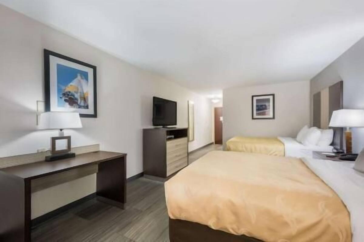 A hotel room with a bed, a desk, a television, and a framed picture on the wall.