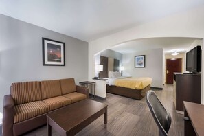 A hotel room with a sofa, a bed, a desk, a chair, and a television.