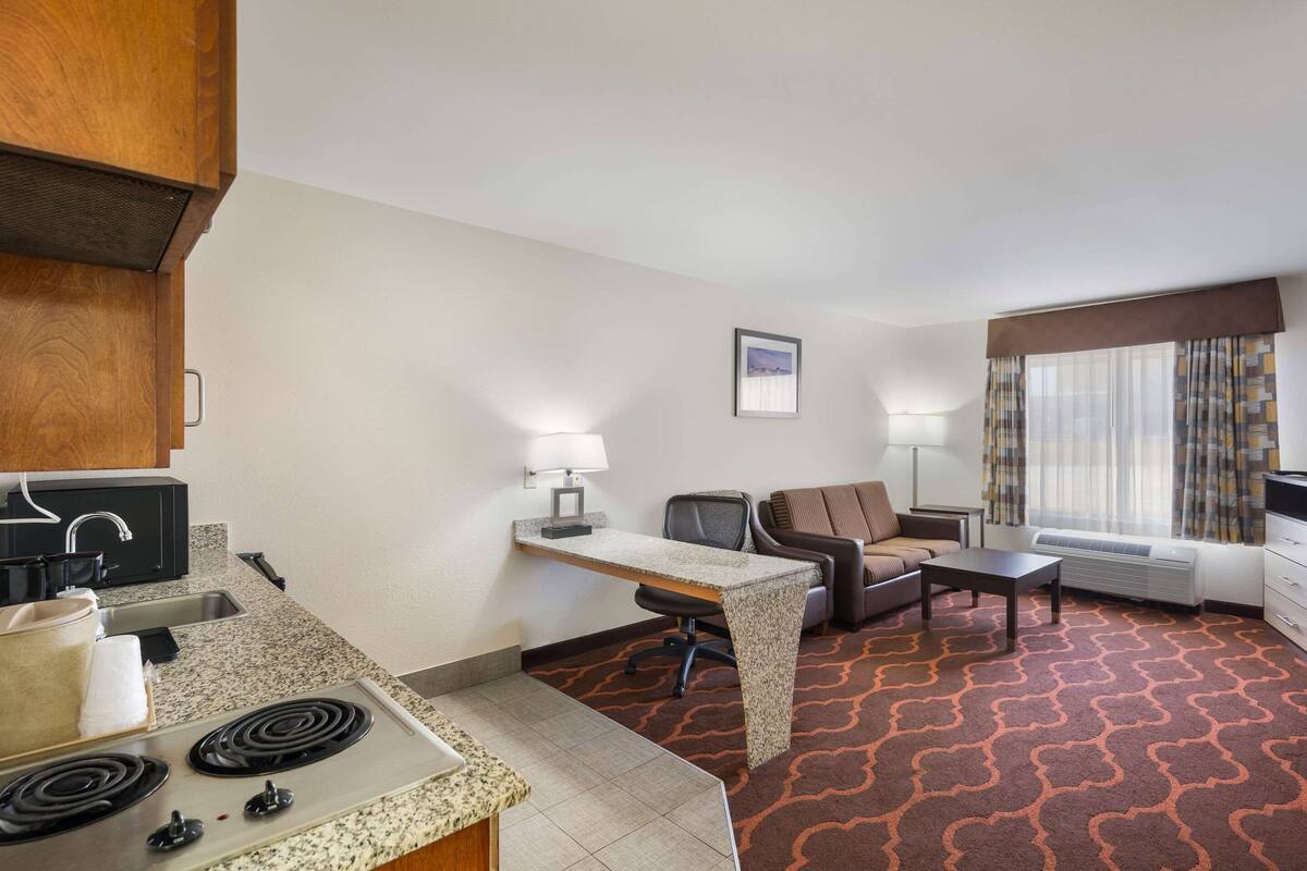 A compact hotel room with a kitchenette, a dining table, a sofa, and a TV.