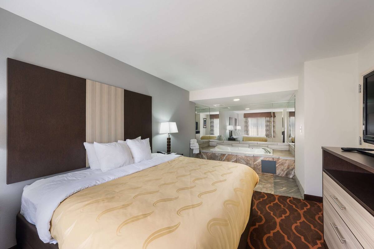 A hotel room with a large bed, a bathroom with a mirror, and a TV on a dresser.