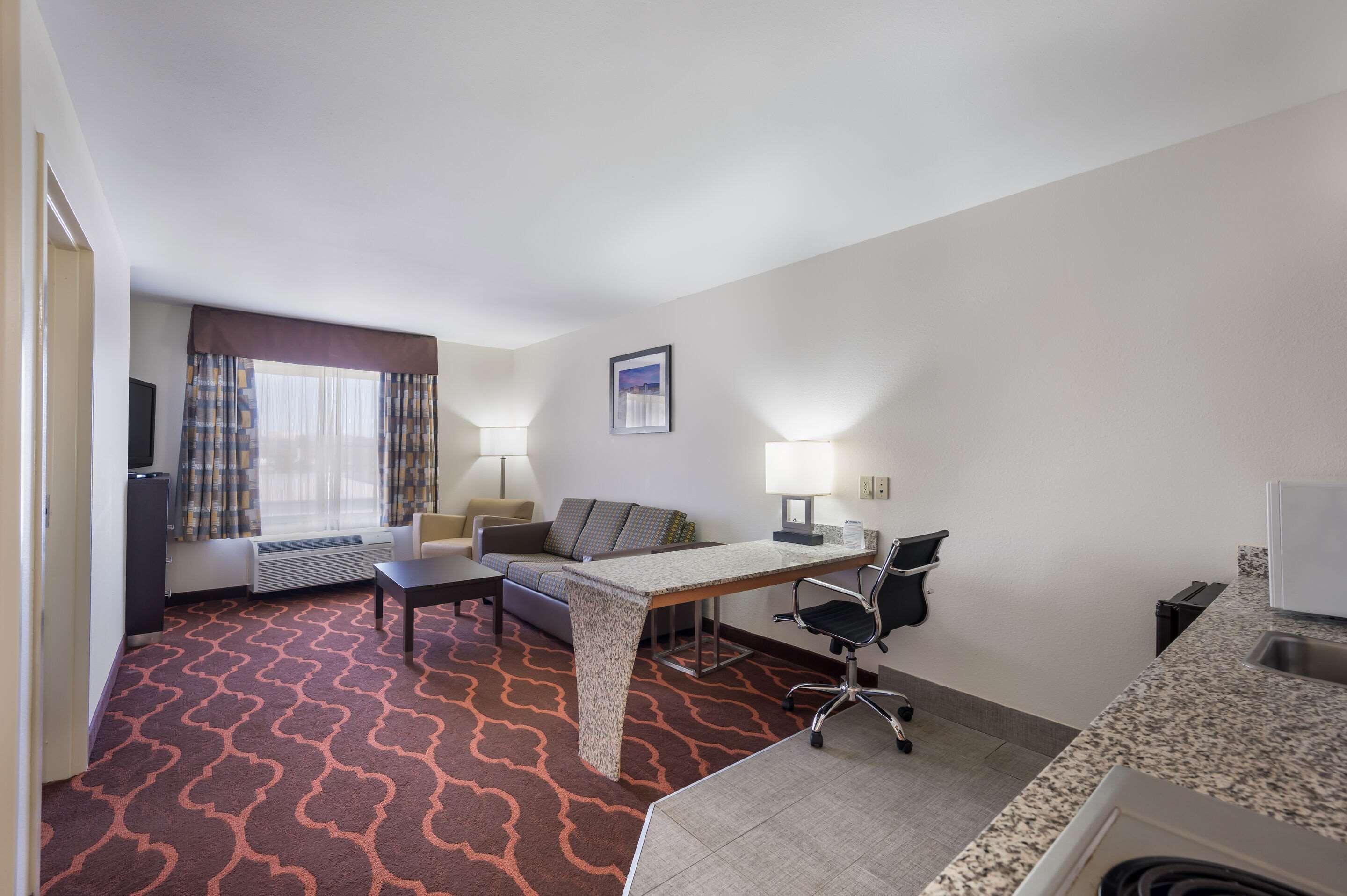 Une chambre d’hôtel équipée d’un canapé, d’un bureau, d’une chaise, d’une télévision, d’une lampe et d’une fenêtre avec des rideaux.