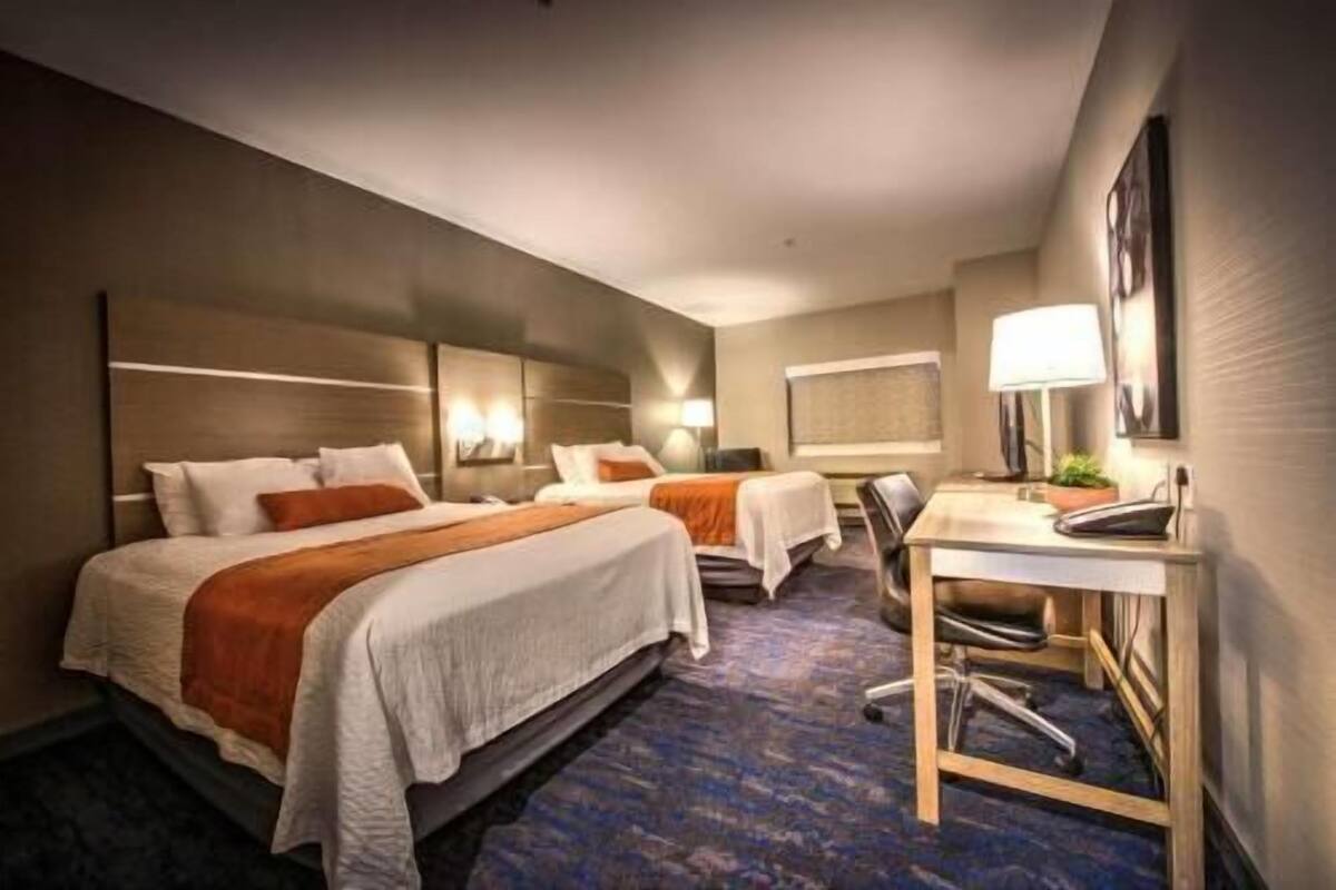 A hotel room with two beds, a desk, and a chair.