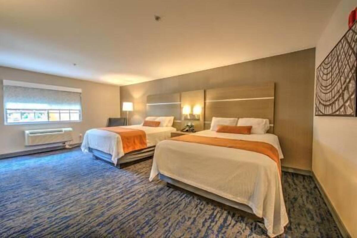 A hotel room with two beds, a window with blinds, a radiator, and a wall-mounted artwork.