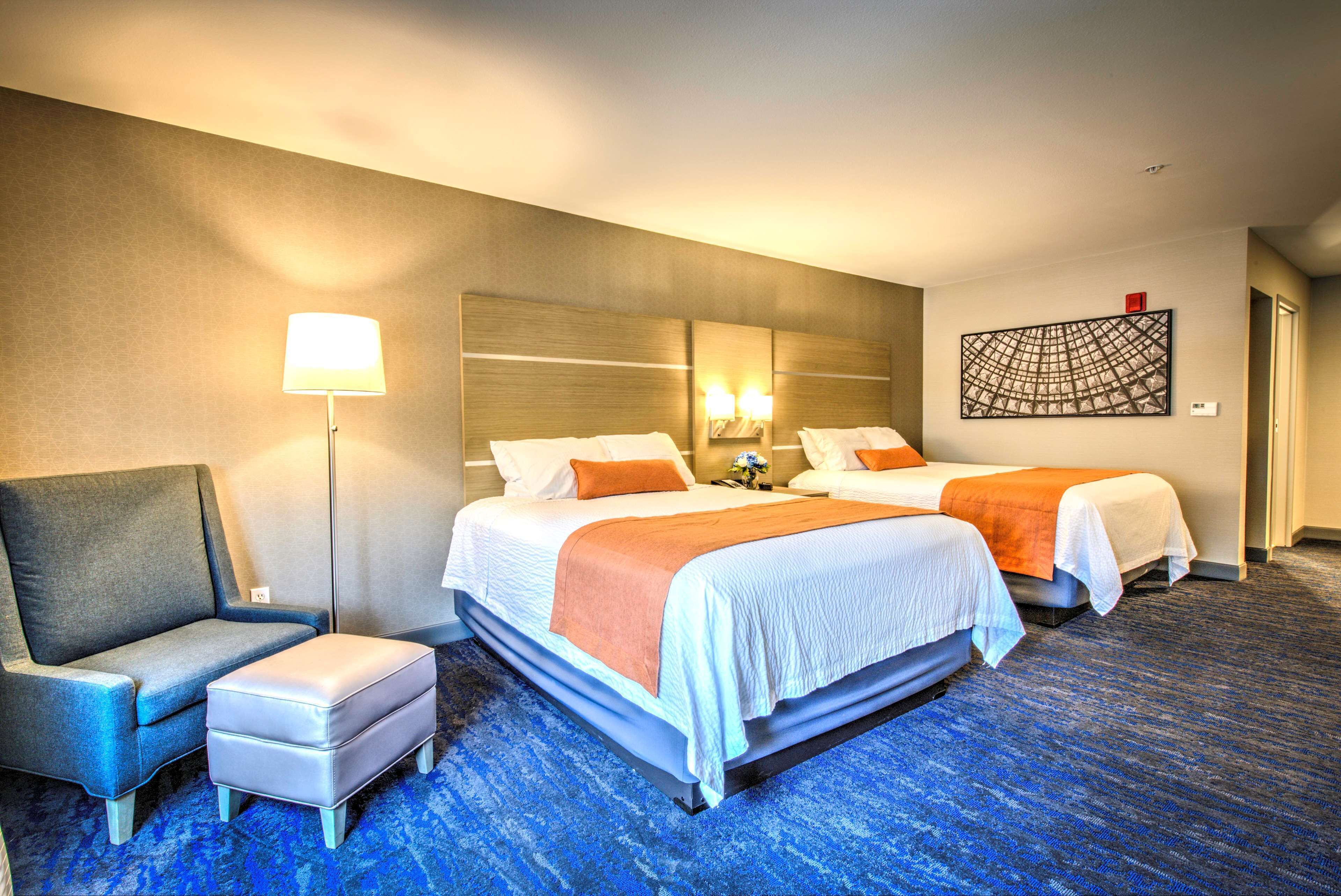A hotel room with two beds, a sofa, a desk, and a lamp.