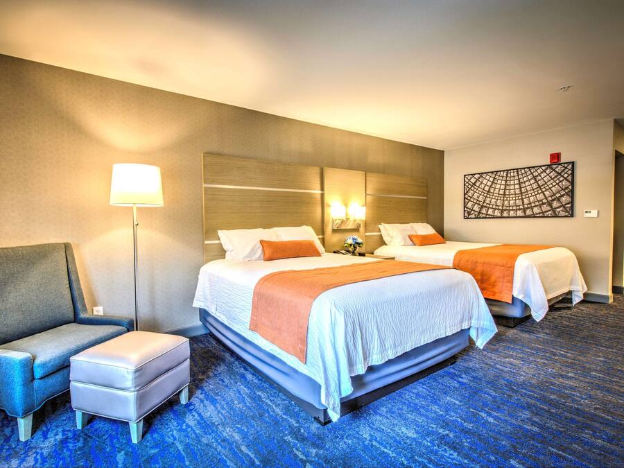 A hotel room with two beds, a sofa, a desk, and a lamp.
