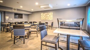 Un espace repas moderne, doté de plusieurs tables et chaises, d’un téléviseur à écran plat fixé au mur et d’une bouche d’aération au plafond.