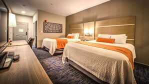 Une chambre d’hôtel avec deux lits, un bureau avec un ordinateur portable, une lampe et une œuvre d’art murale.