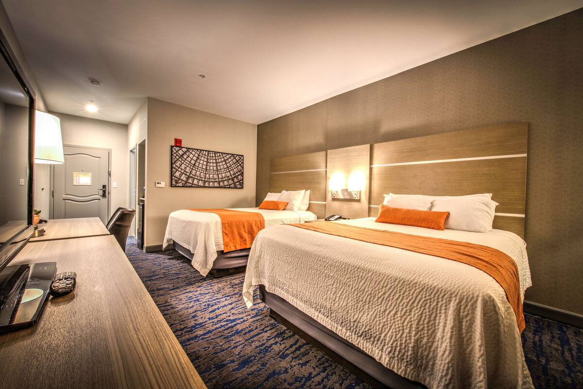 A hotel room with two beds, a desk with a laptop, a lamp, and a wall art piece.