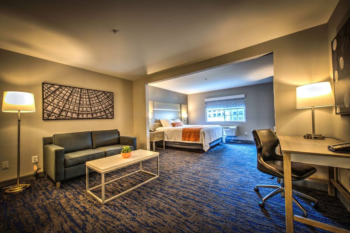 A hotel room with a sofa, a desk, a bed, and a large window.