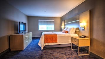 Habitación de hotel con cama, televisor sobre una cómoda de madera, mesita de noche con lámpara y ventana con vistas.