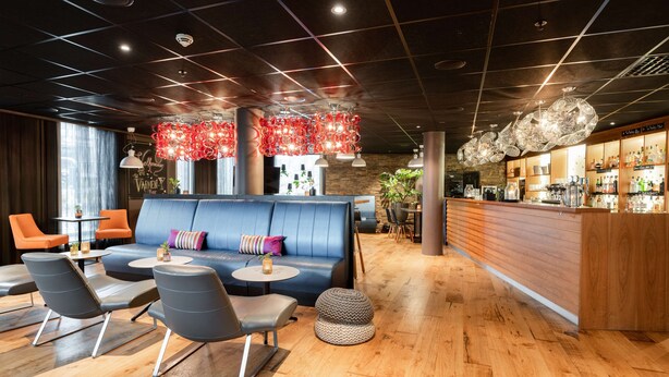 A modern lounge area with a blue sofa, grey chairs, and a wooden bar counter. - Scandic Stavanger City (Stavanger)