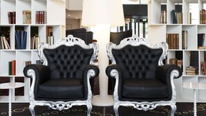A library with two ornate black and white chairs, a large white lamp, and bookshelves filled with books. - Scandic Stavanger City (Stavanger)