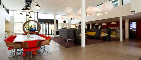 A spacious lobby with a modern dining area, large windows, and contemporary lighting fixtures.