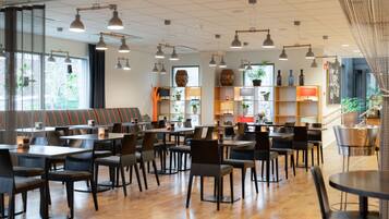 Ein geräumiges Café mit mehreren Tischen und Stühlen, Holzböden sowie Regalen mit Pflanzen und Dekorationsobjekten.