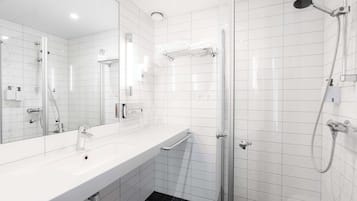 Ein modernes Badezimmer mit einem großen Spiegel, einem weißen Waschbecken, einer Dusche mit Handbrause und einer Glastrennwand.