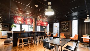 A modern restaurant with wooden flooring, black and orange chairs, and a bar area. - Scandic Stavanger City (Stavanger)