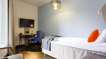 A modern bedroom with a bed, a desk with a chair, a television, and a hanging light fixture.