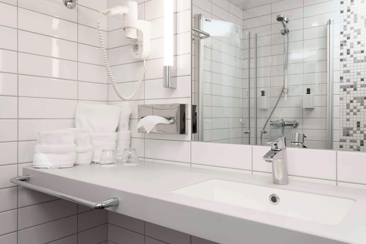 A modern bathroom with a large mirror, a white sink, a handheld showerhead, and neatly folded towels.