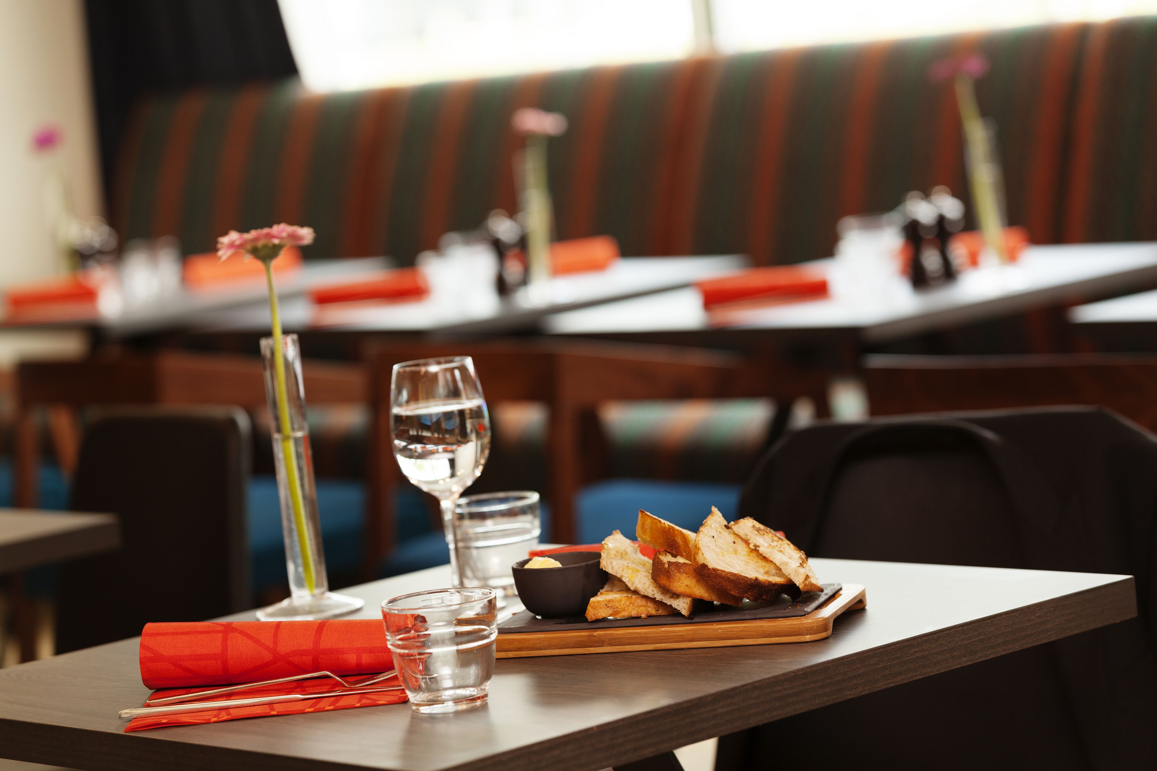 A dining table with a glass of water, a glass of wine, a small bowl of butter, and a plate of bread.