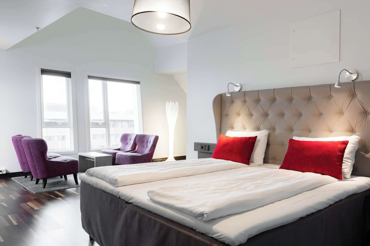 A hotel room with a large bed, two chairs, a desk, and a window.