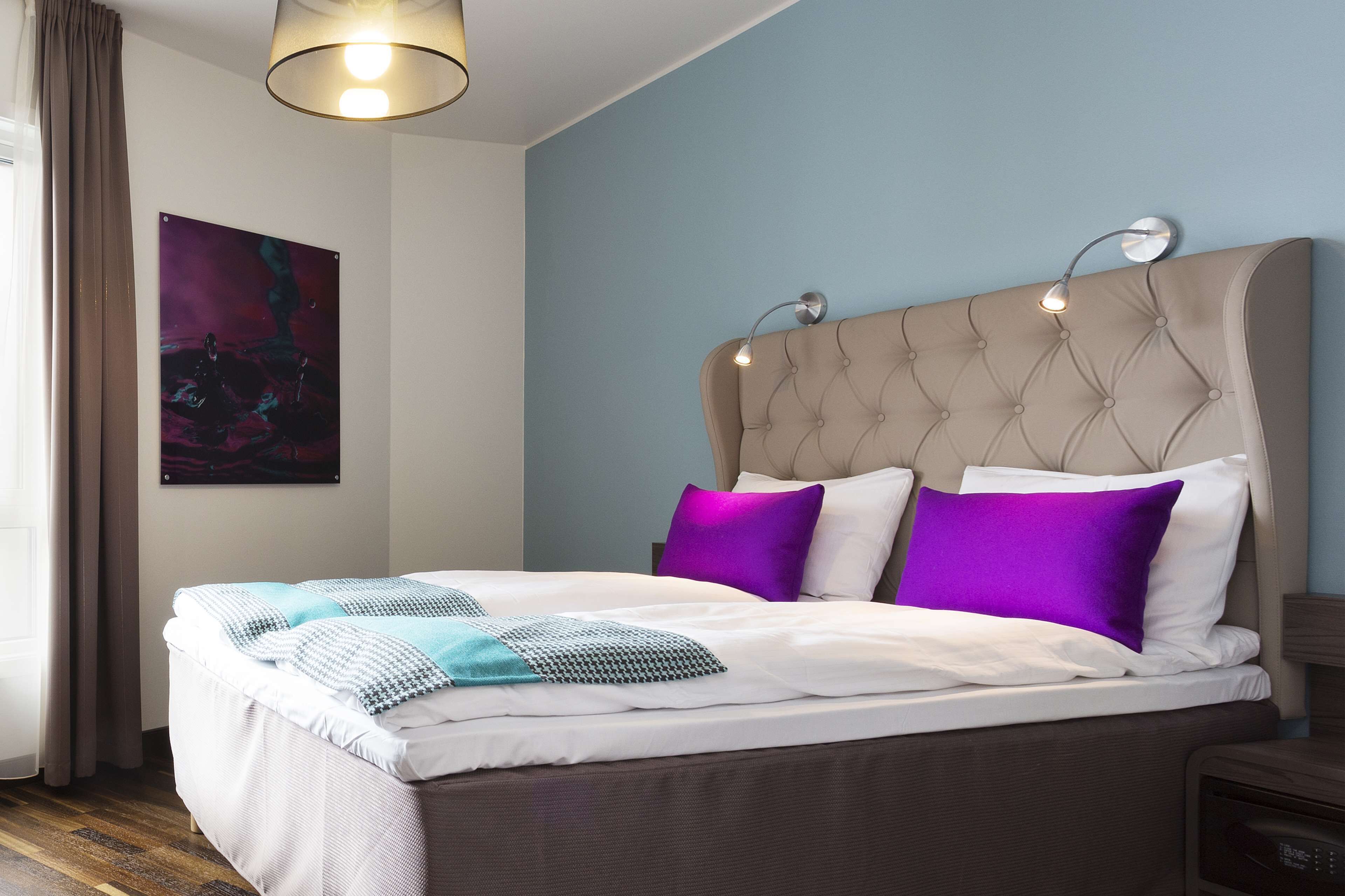 A neatly made bed with a tufted headboard, a bedside table, and a wall-mounted lamp.