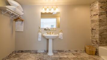 Une salle de bain avec un lavabo sur colonne, un miroir au-dessus, et une zone douche située à droite.