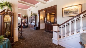 A grand hallway with a wooden staircase, a large clock, and a bookshelf. - Hotel La Rose (Santa Rosa)