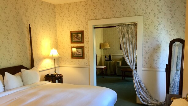 A hotel room with a large bed, a bedside lamp, a chair, a small table, and a mirror.