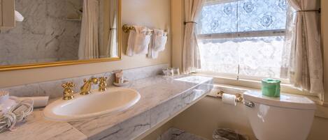A bathroom with a marble vanity, two sinks, a toilet, and a window with patterned curtains.