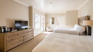 A hotel room with a large bed, a smaller bed, a TV on a wooden dresser, and a chair near the window.