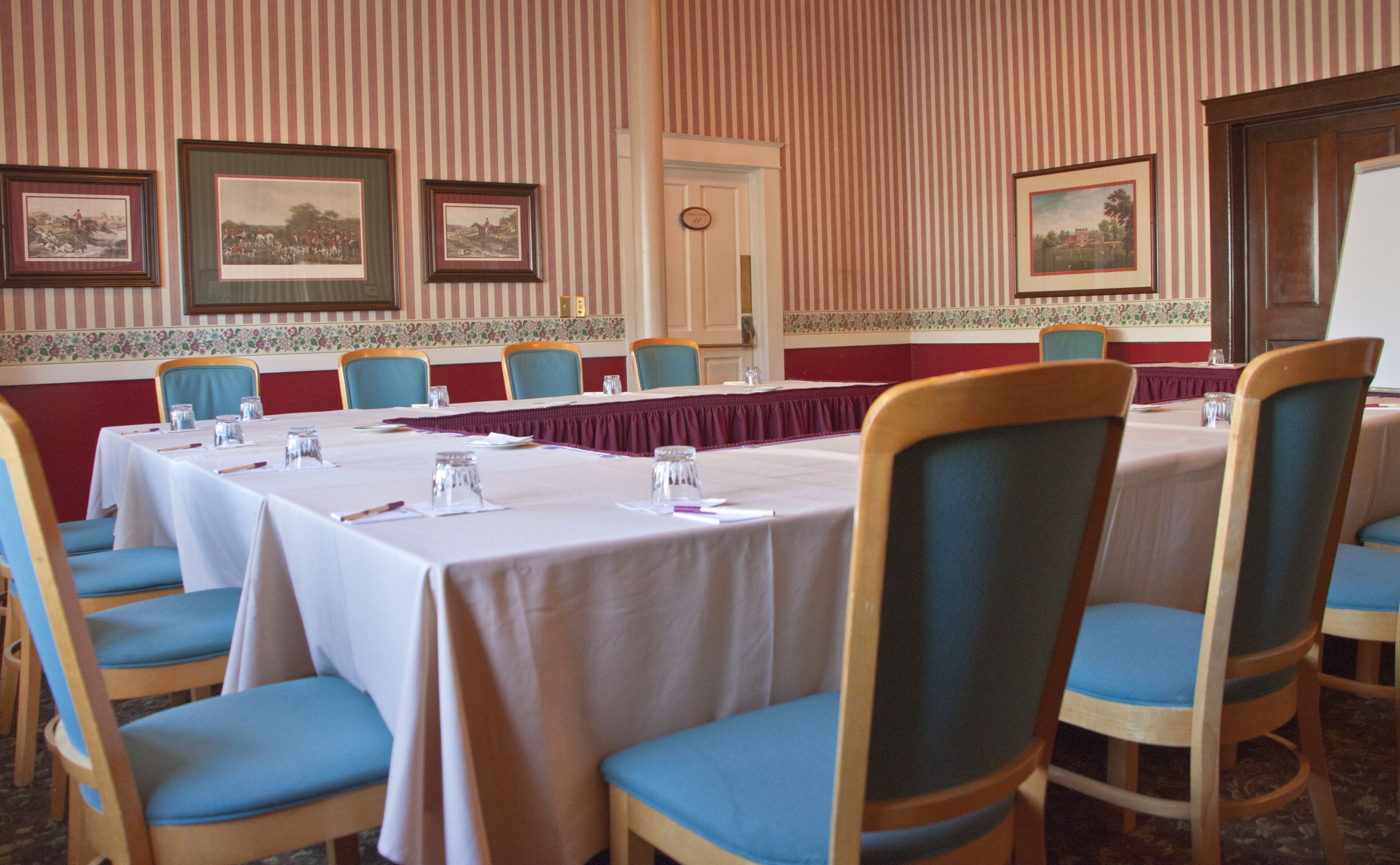 A conference room with tables and chairs, framed pictures on the walls, and a door with a number.
