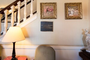 A staircase with a lamp, two framed floral paintings, and a plaque on the wall.