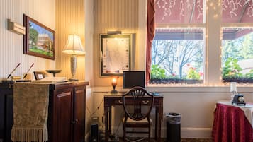 Habitación con escritorio, silla, lámpara, computadora y ventana con vistas a árboles y flores.