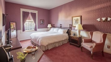 A hotel room with a bed, a desk with a computer, a chair, and a window with curtains.