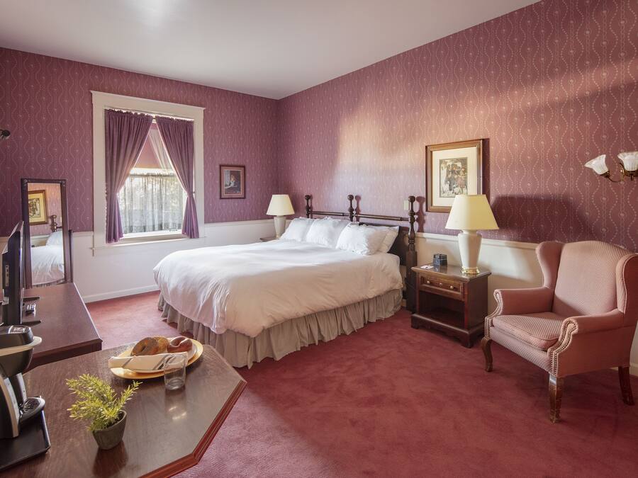 A hotel room with a bed, a desk with a computer, a chair, and a window with curtains.