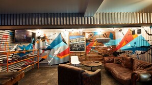 A cozy lounge area with a brown leather sofa, a white chair, and a small round table. - St Christopher's Inn, Camden - Hostel (London)