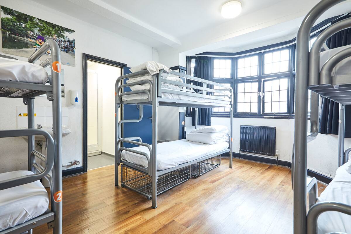 A bunk room with metal bunk beds, a wooden floor, a window with curtains, and a radiator.