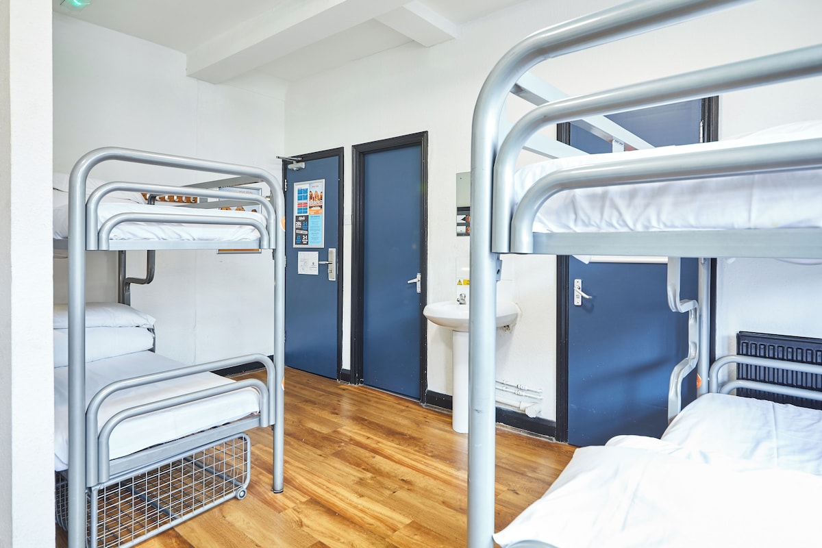A bunk bed room with a wooden floor, a sink, and a door with a poster.