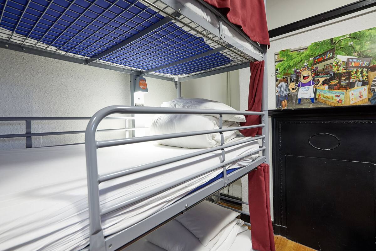 A bunk bed room with a metal frame, white bedding, and a black wardrobe.