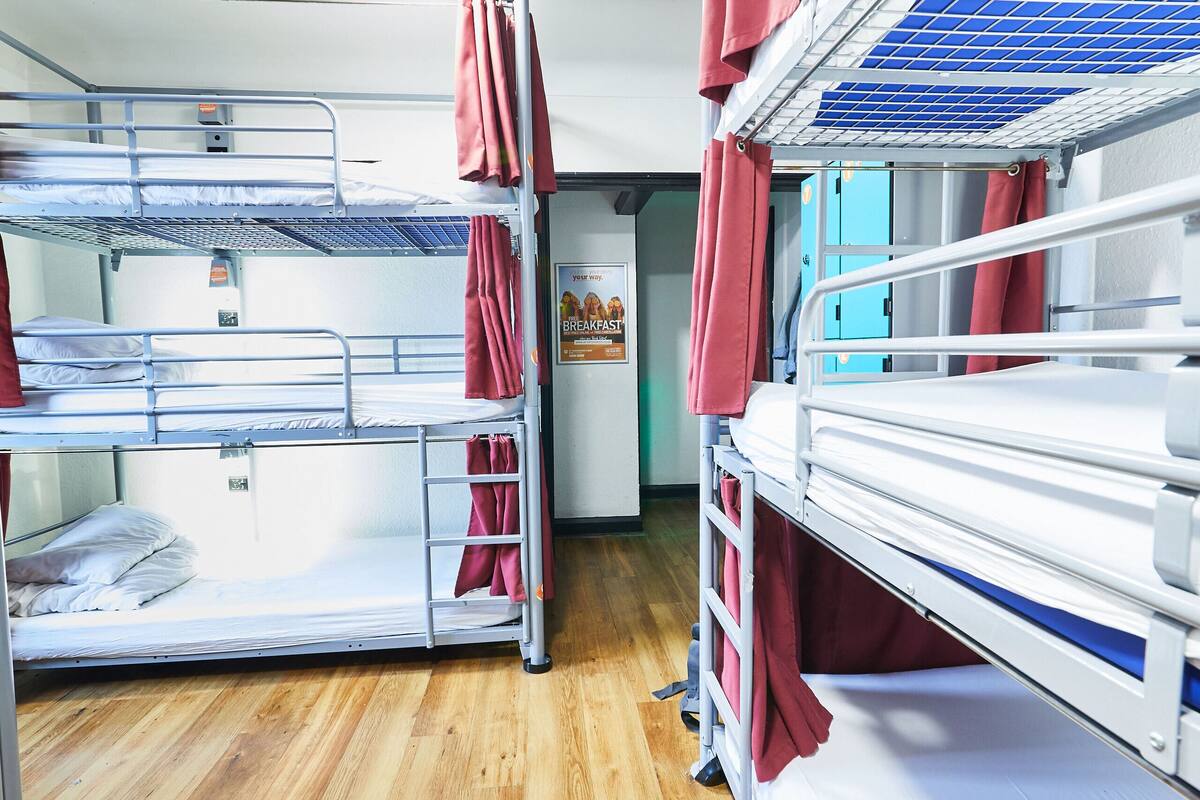 A dormitory room with bunk beds, wooden flooring, and a poster on the wall.