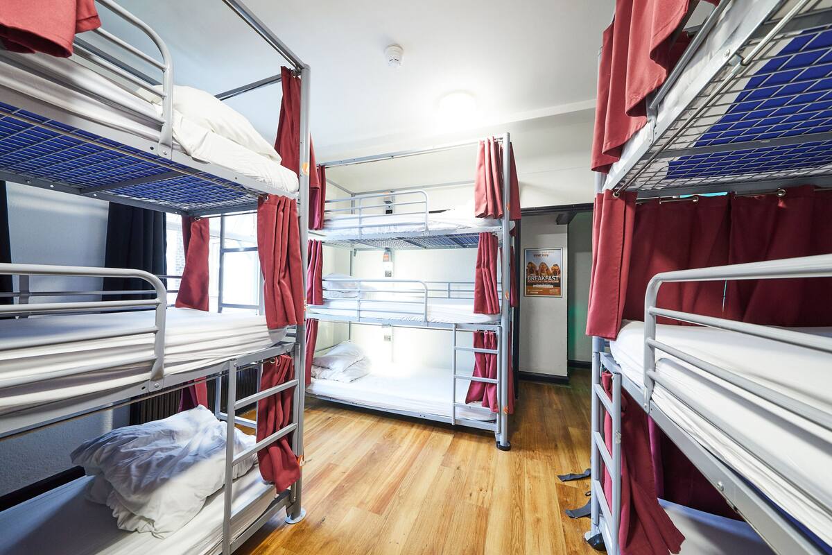 A dormitory room with bunk beds, a wooden floor, and a poster on the wall.