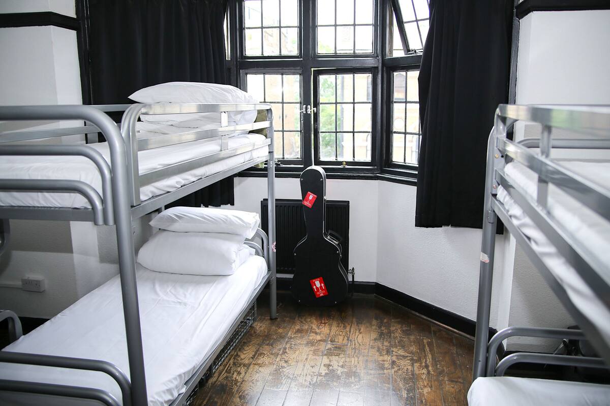 A dormitory room with bunk beds, a guitar, and a window with black curtains.