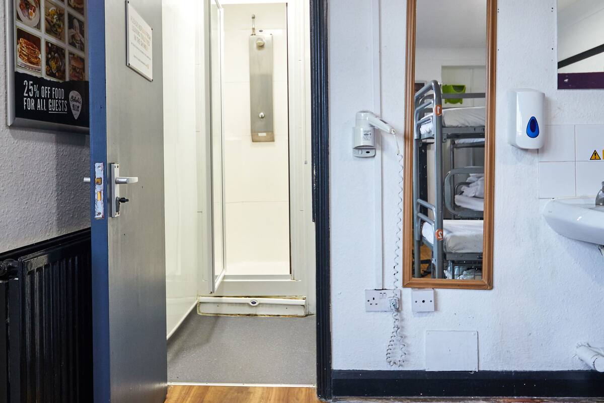A hotel corridor with a wooden floor, a door leading to a room, a mirror, a sink, and a wall-mounted sign offering a discount on food for guests.