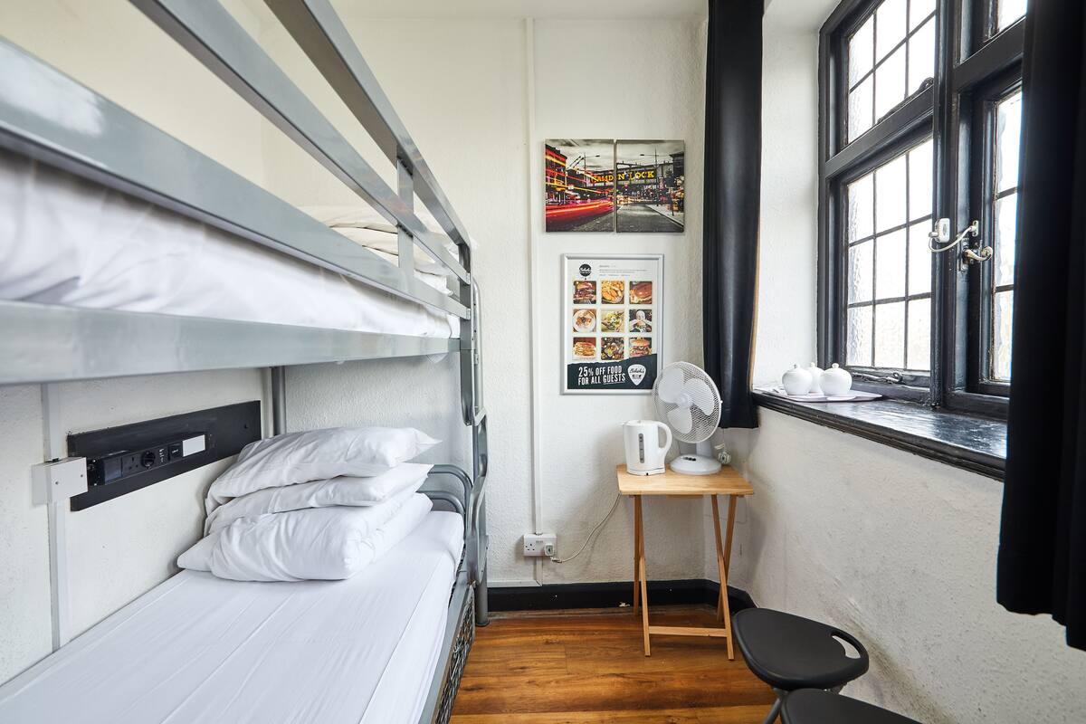 A bunk bed room with a small table, a fan, and a window with curtains.