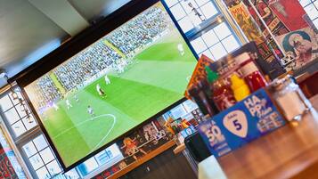 A large screen displaying a sports event in a venue with a high ceiling and large windows.