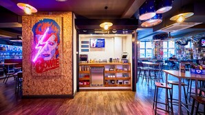 A restaurant interior with a bar area, wooden flooring, and a neon sign on the wall. - St Christopher's Inn, Camden - Hostel (London)