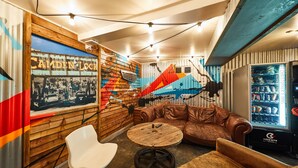 A cozy lounge area with a vintage wall mural, leather seating, a vintage table, and a beverage vending machine. - St Christopher's Inn, Camden - Hostel (London)