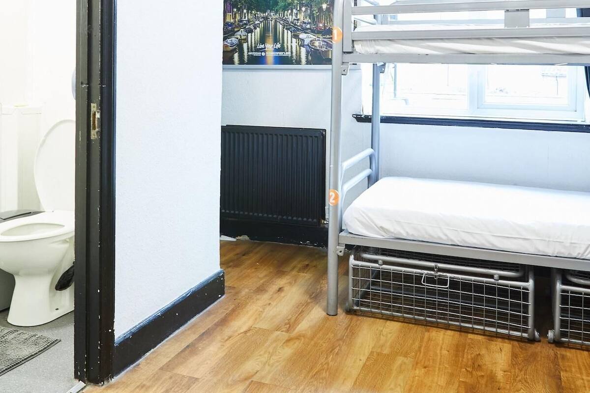 A bunk room with a bunk bed, a toilet, a fire exit sign, and a poster of a cityscape.