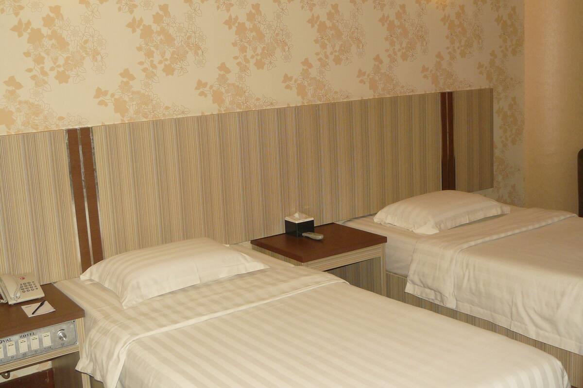 Ein Hotelzimmer mit zwei Betten, einem Nachttisch mit Telefon und Taschentuchbox sowie einem gestreiften Kopfteil.