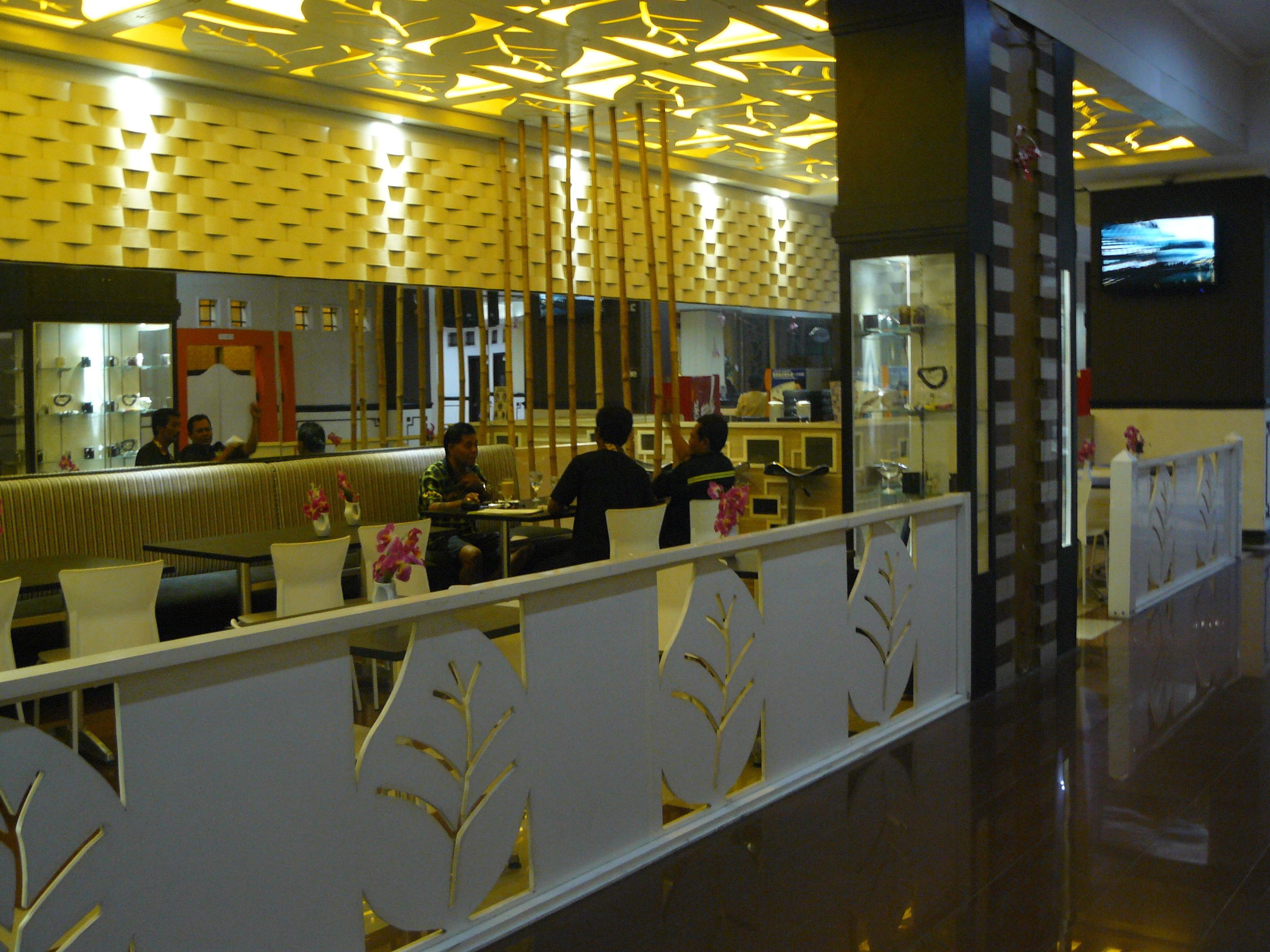 Un restaurant moderne doté d’un plafond aux motifs géométriques, d’un comptoir avec un miroir et d’un espace salon agrémenté d’une cloison décorative.